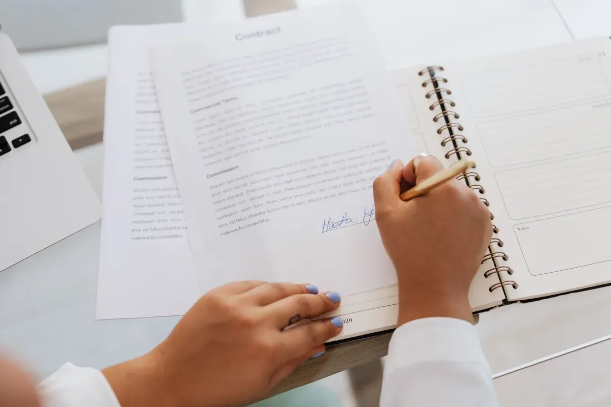 Pessoa assinando um documento com caneta ao lado de um caderno