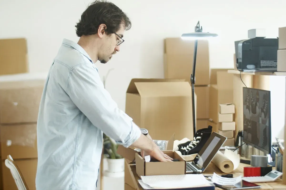 Empreendedor embalando produtos em casa ao lado do notebook, depois de começar a vender pela internet