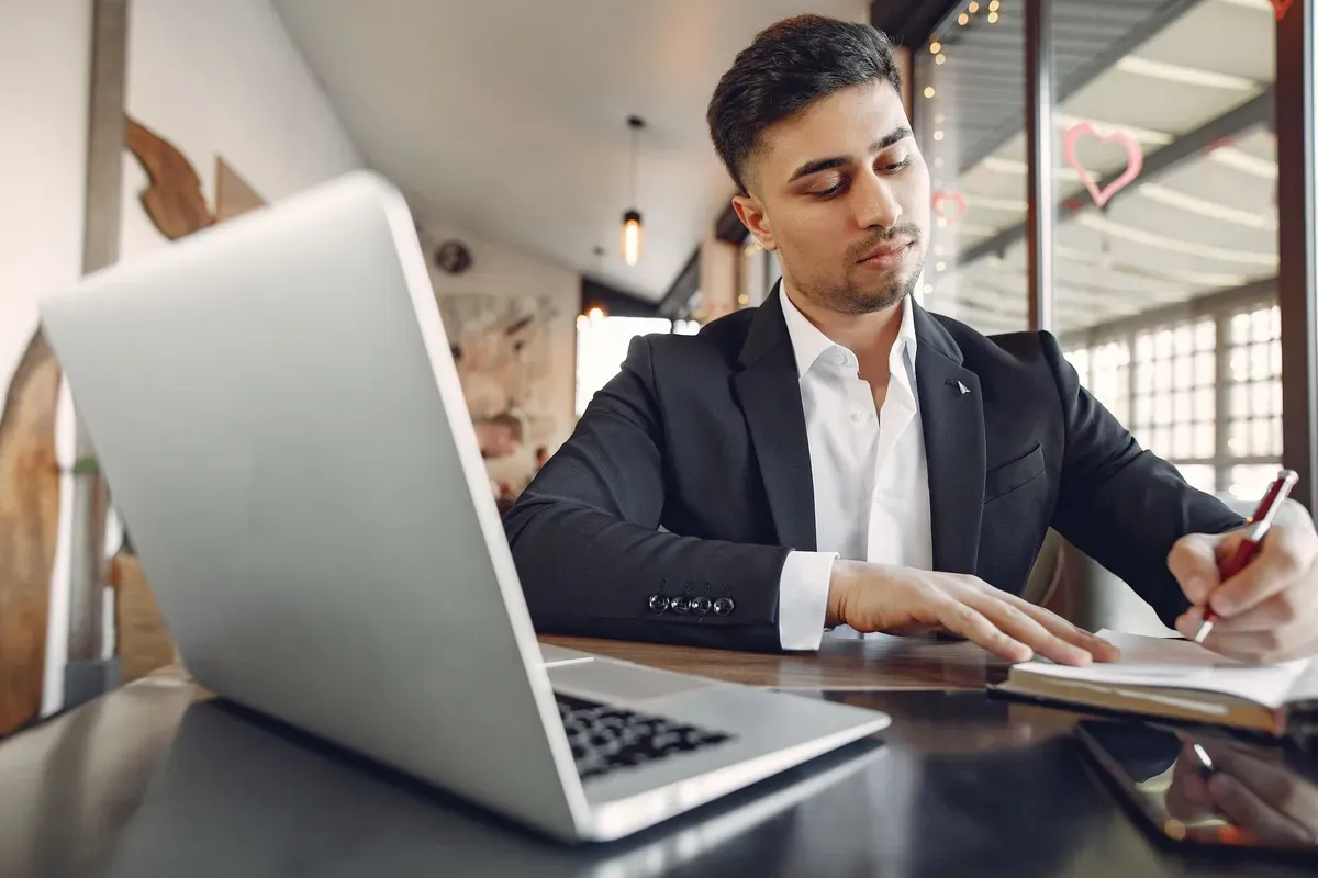 Empresário de terno fazendo anotações ao lado do notebook em um café
