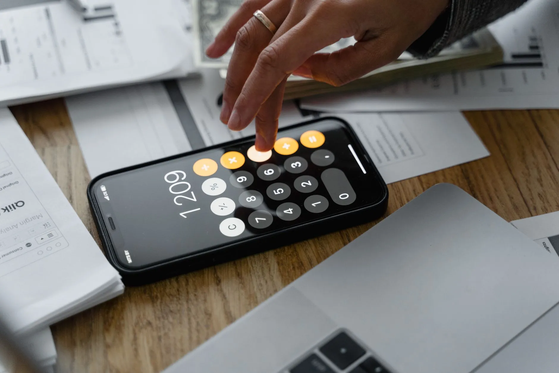 Mão usando a calculadora do celular sobre documentos e notebook