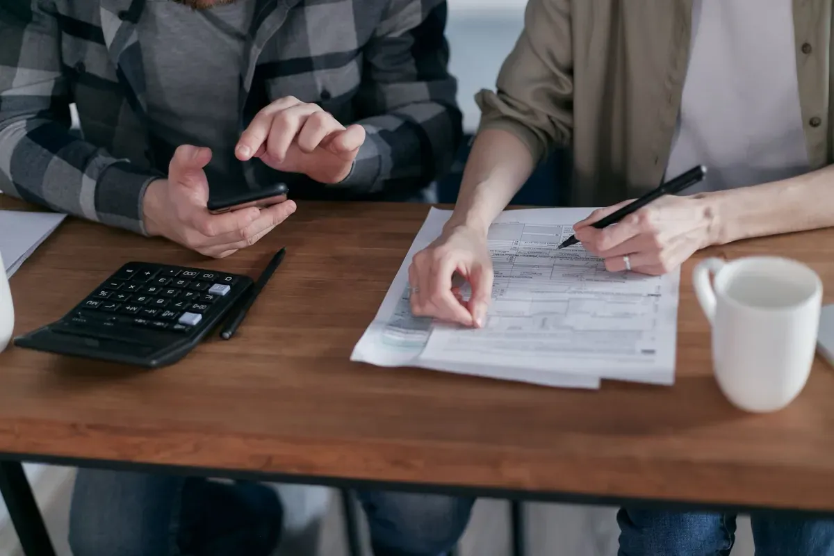 Duas pessoas conferindo formulários de imposto com uma calculadora