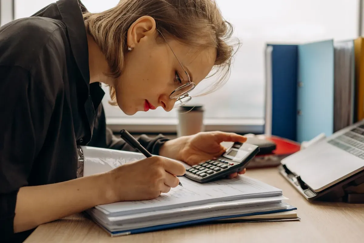 Mulher fazendo contas com calculadora e anotando em um caderno