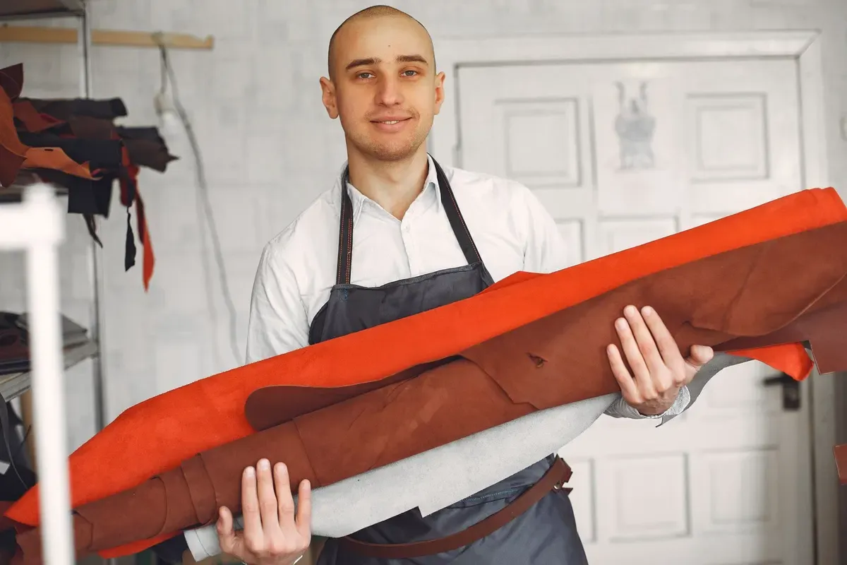 Artesão sorridente de avental segurando rolos de tecido no seu ateliê