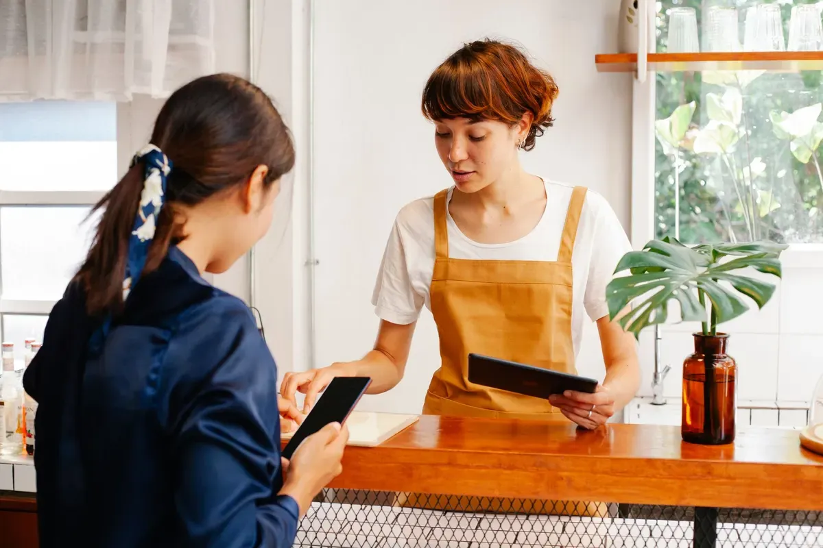 Duas atendentes no balcão de uma cafeteria conferindo pedidos no tablet