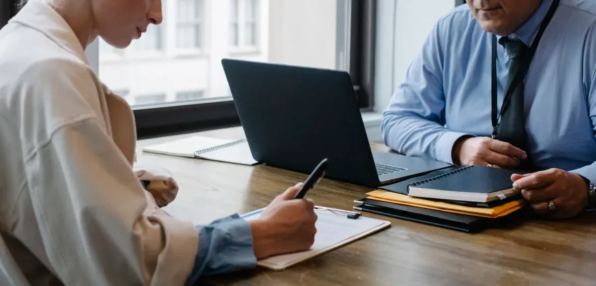 Colegas assinando documentos de admissão sobre uma mesa com notebook