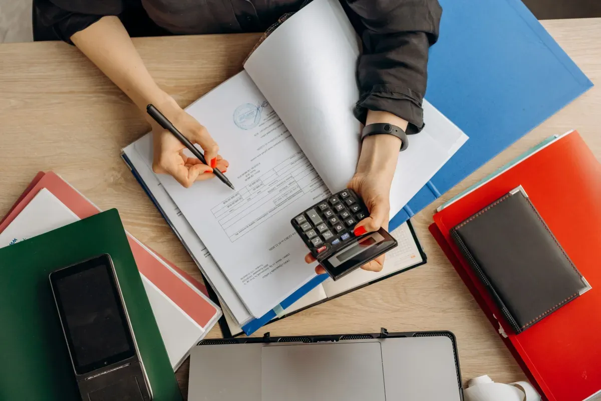 Pessoa fazendo contas com calculadora e caderno sobre a mesa