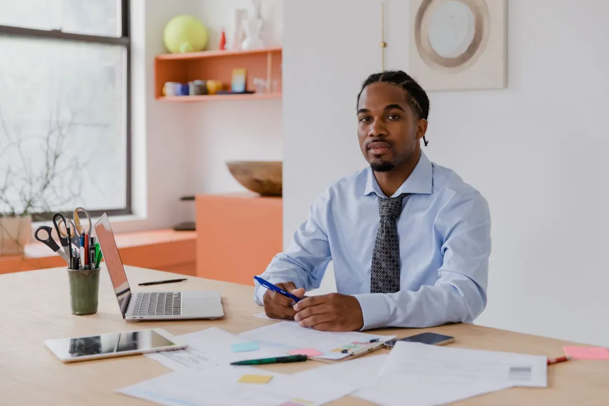 Sócio de camisa e gravata à mesa do escritório com notebook, papéis e caneta na mão