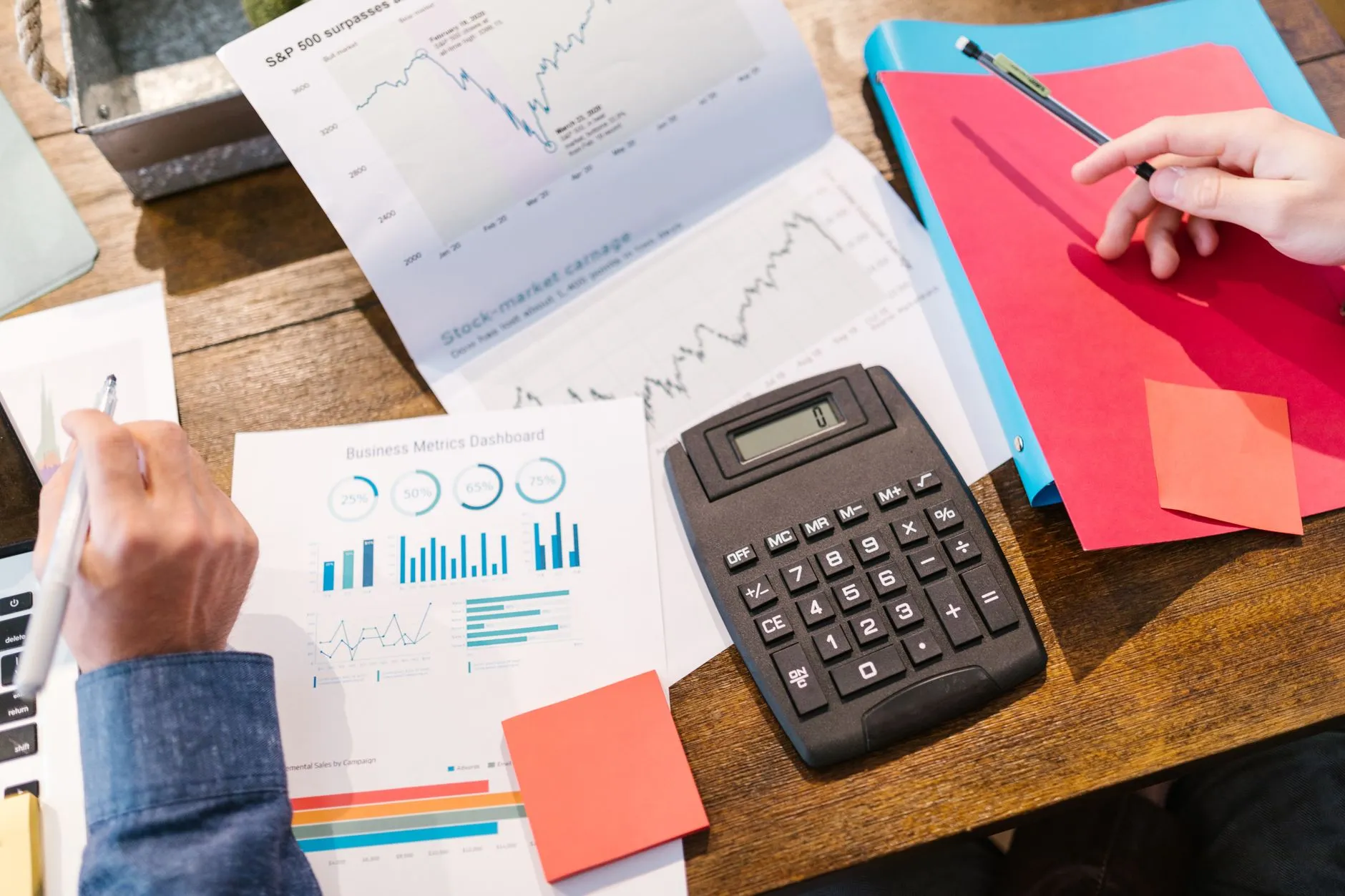 Mesa com gráficos, calculadora e papéis coloridos durante uma análise financeira