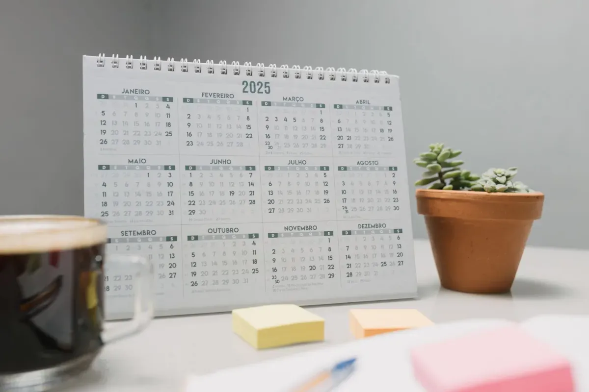 Calendário de 2025 sobre a mesa, com vaso de planta e bloco de notas