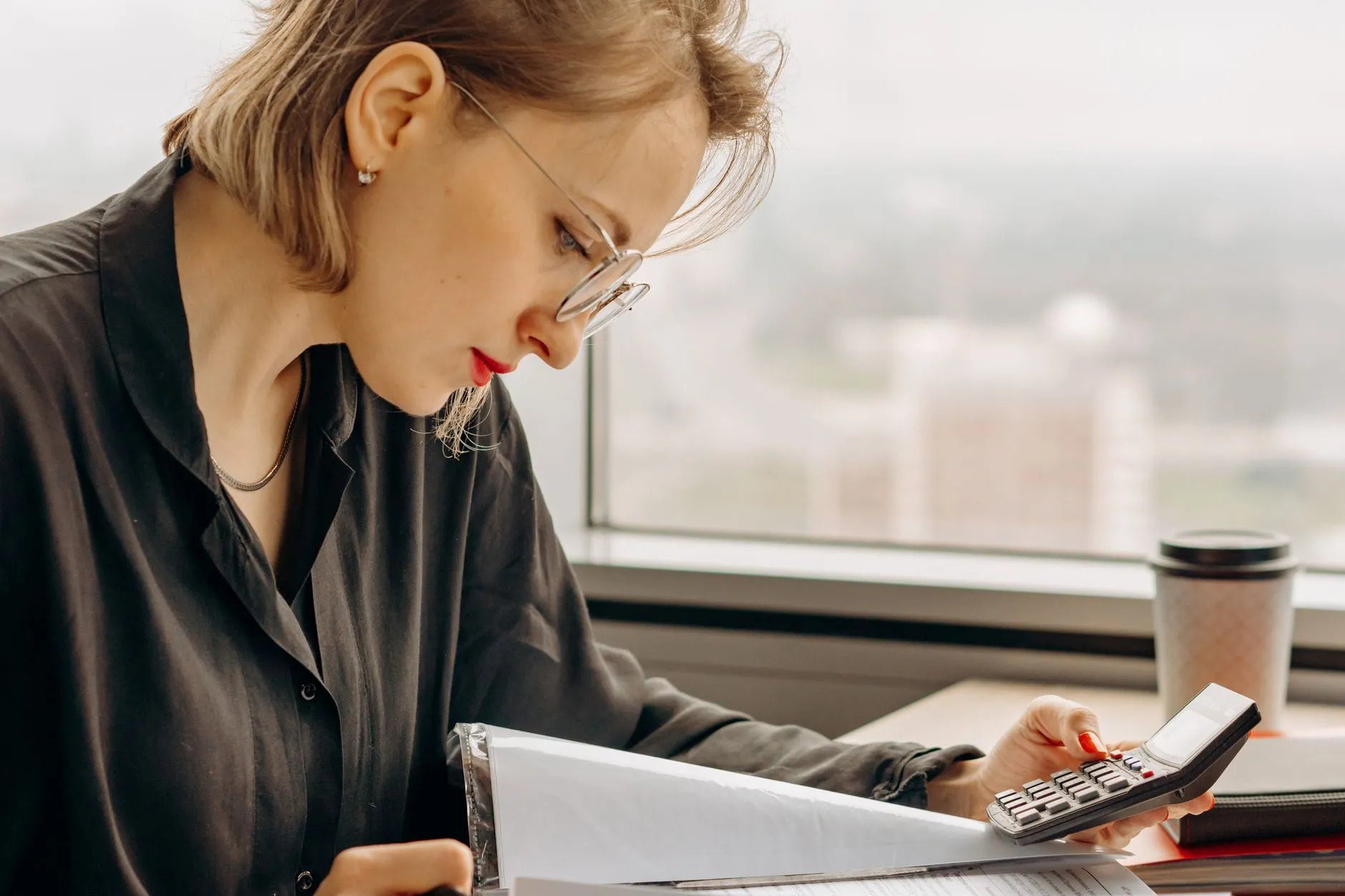 Mulher de óculos fazendo contas com calculadora e documentos